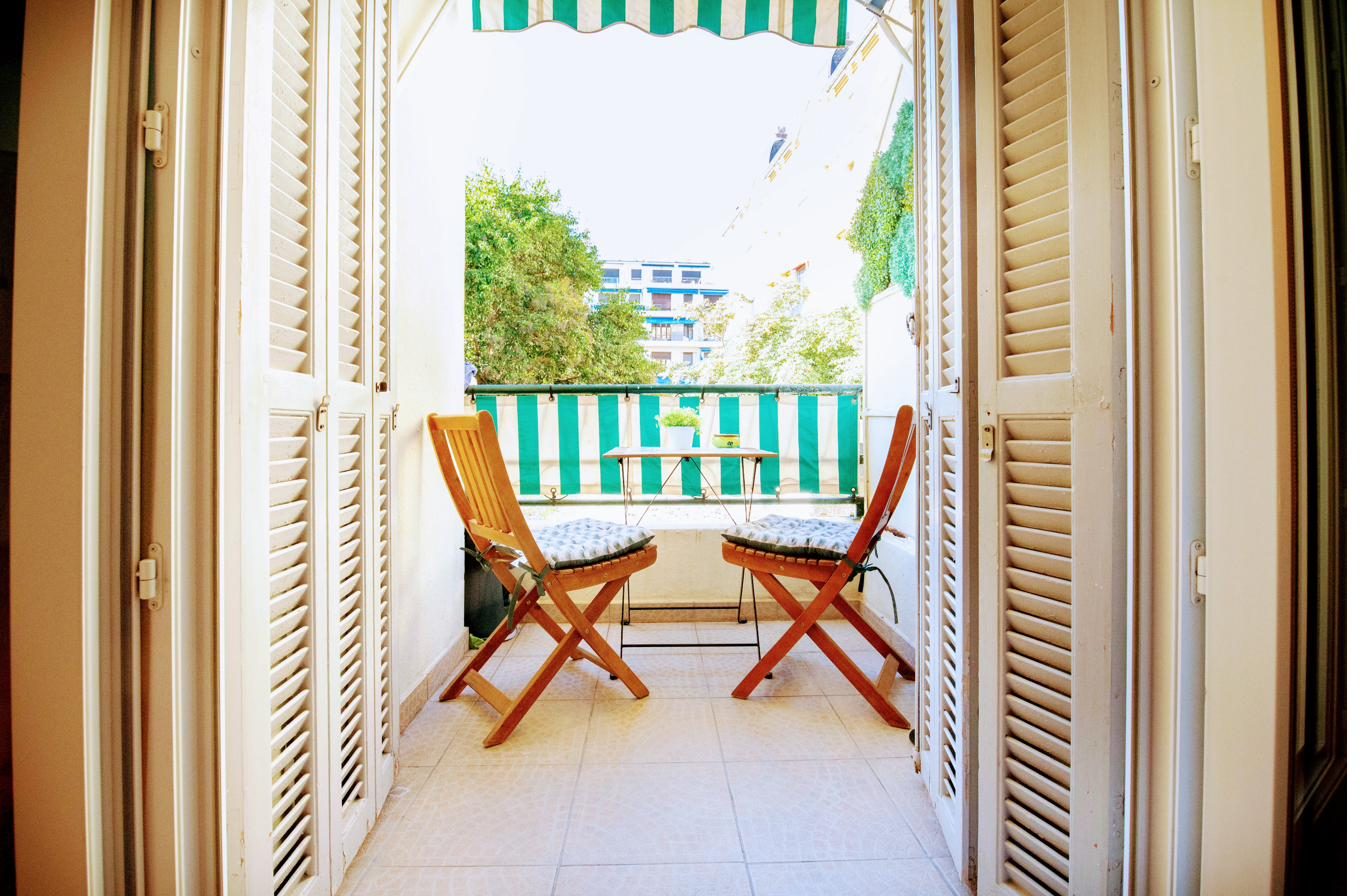 Balcon privatif ouvert sur le quartier, table et chaises sous le store