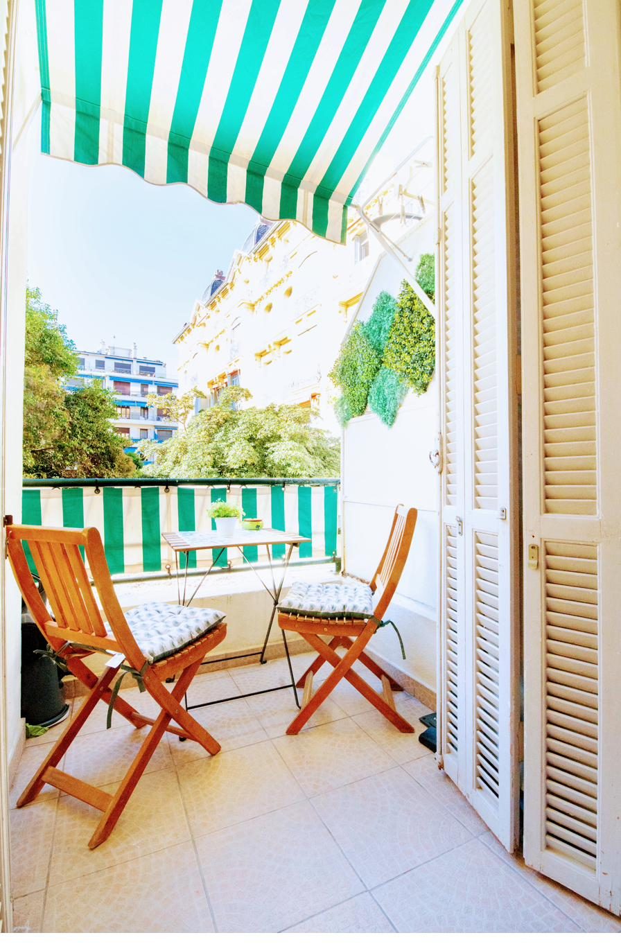 Balcon privatif avec store rayé vert donnant sur un jardin